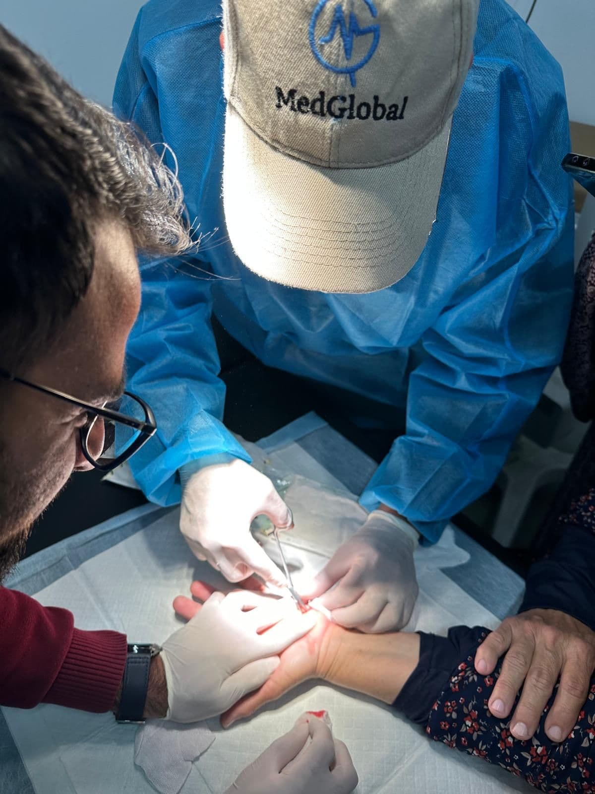 Volunteer surgeon in a MedGlobal cap treating a patient's hand